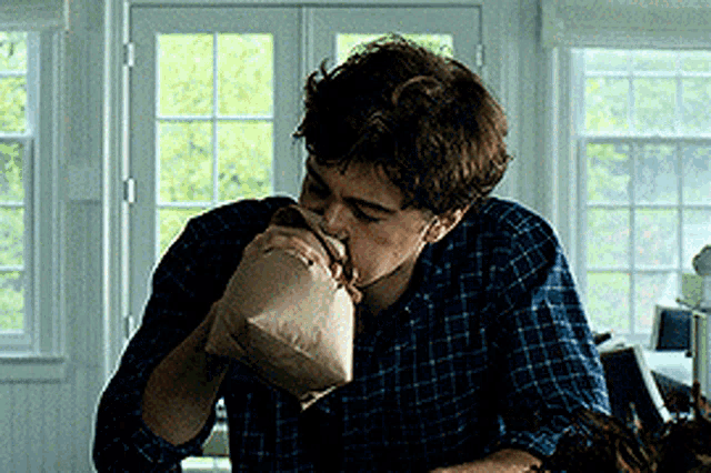 a young man in a plaid shirt is drinking from a bag
