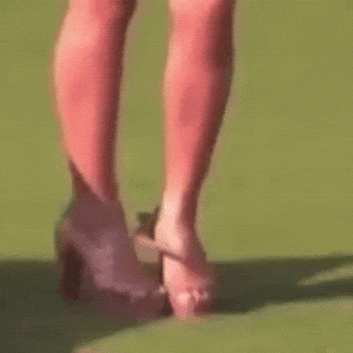 a woman is walking barefoot on a green field while a pair of shoes are on the ground .