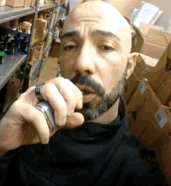 a bald man with a beard is smoking an electronic cigarette in a warehouse
