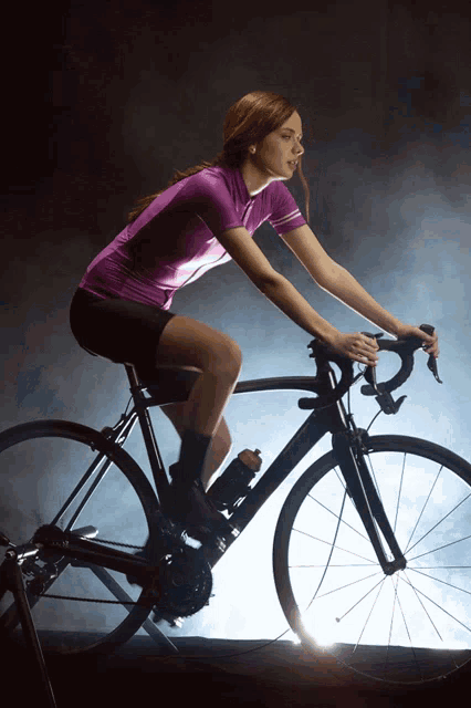 a woman in a purple shirt is riding a black bicycle