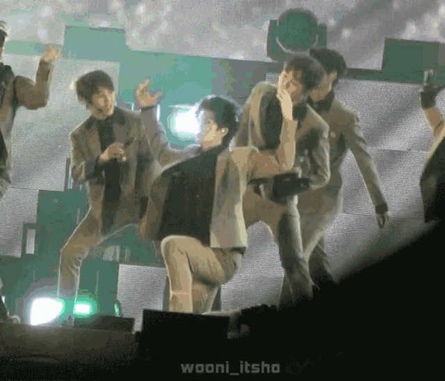 a group of men are dancing on a stage with wooni_itsho in the corner