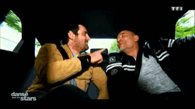 two men are sitting in the back seat of a car and one of them is pointing a gun at the other ..