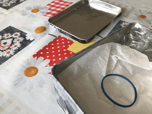a blue rubber band sits on a tray on a table cloth with daisies on it