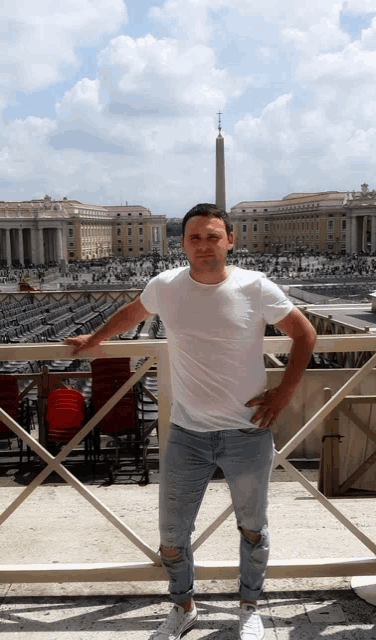 a man in a white shirt and jeans stands in front of a large building