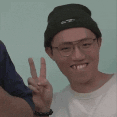 a young man wearing glasses and a beanie is giving a peace sign