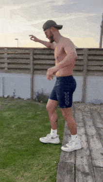 a shirtless man is standing on a wooden deck in front of a fence .