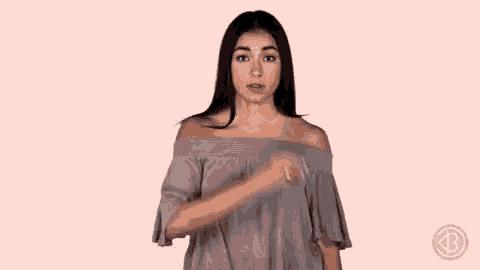 a woman in a gray off the shoulder top is making a gesture with her hand .