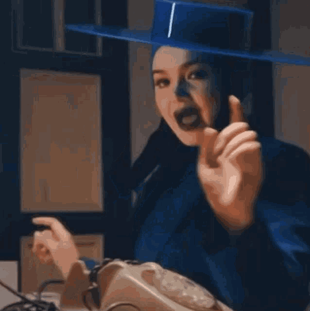a woman in a blue hat is talking on a telephone and making a funny face .