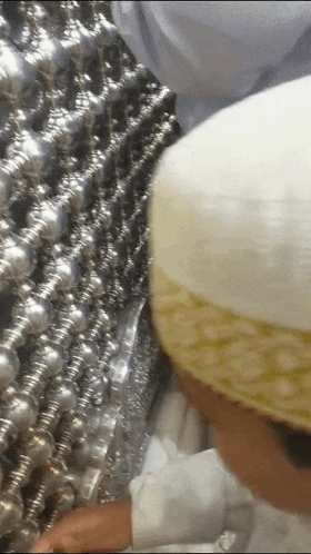 a man wearing a white hat looks at a metal item