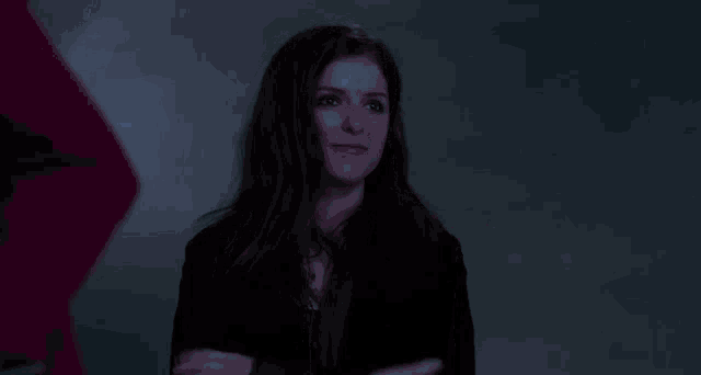a woman in a black jacket is covering her mouth with her hands in a dark room .