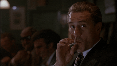 a man in a suit smoking a cigarette in a dark room