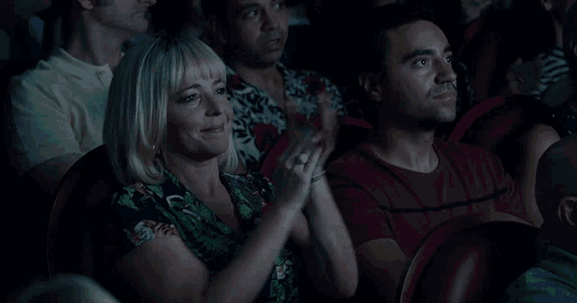 a man and a woman applaud while watching a movie in a theater