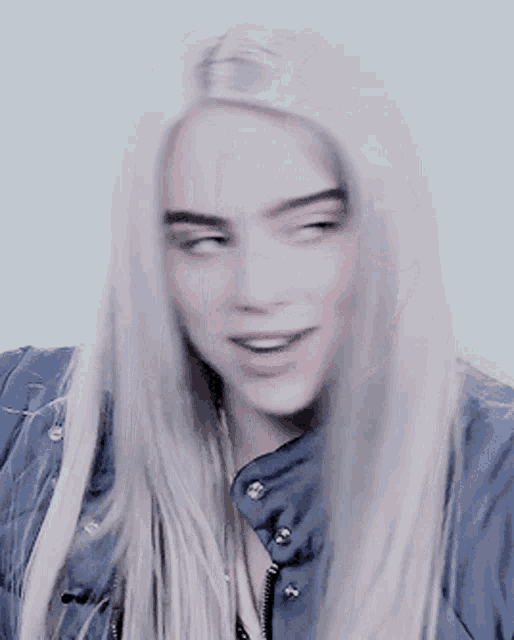 a woman with long white hair wearing a blue jacket is smiling