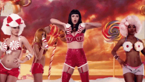a woman in a red bra and shorts is surrounded by other women in candy costumes .