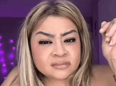 a woman with blonde hair and a purple background is making a funny face with her hand .