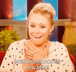 a woman is smiling and holding her hands to her chest while saying merci beaucoup ma mimi .