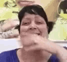 a woman in a blue shirt is smiling and covering her mouth with her hands .