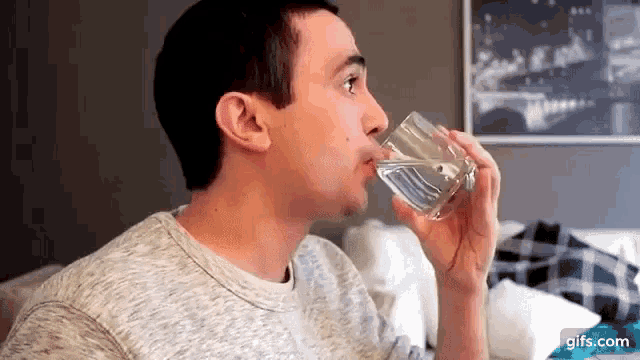 a young man is drinking a glass of water .