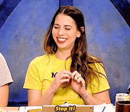 a woman in a yellow shirt is sitting at a table with a cardboard sign that says stop it