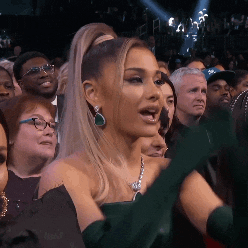 a woman with a ponytail and green earrings stands in a crowd of people