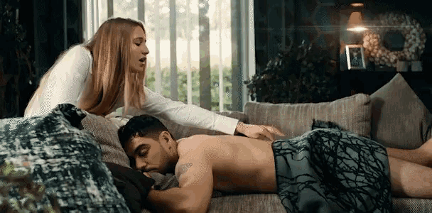 a shirtless man laying on a couch with a woman standing behind him