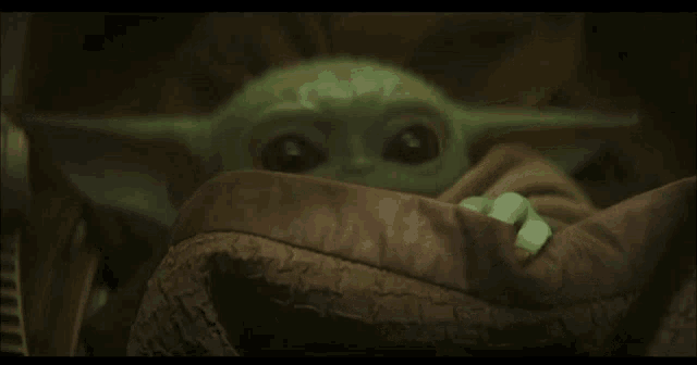 a baby yoda is wrapped in a brown blanket .