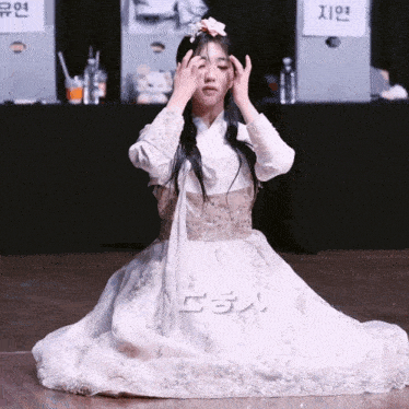 a woman in a white dress is kneeling down in front of a sign that says ' a ' on it