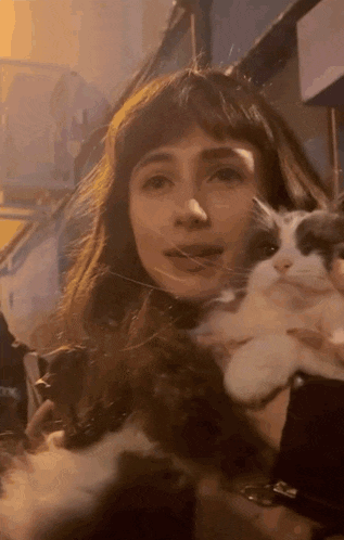 a woman is holding a white and black cat in her arms