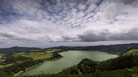 a lake surrounded by mountains and trees with a cloudy sky above it