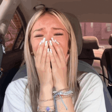 a woman covering her mouth with her hands while sitting in a car