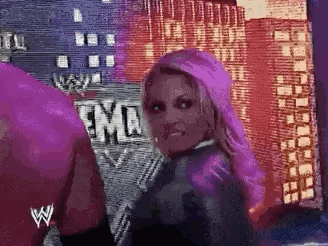 a woman with purple hair is standing in front of a sign that says wwe on it .