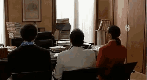 three people are sitting at a desk in a room .