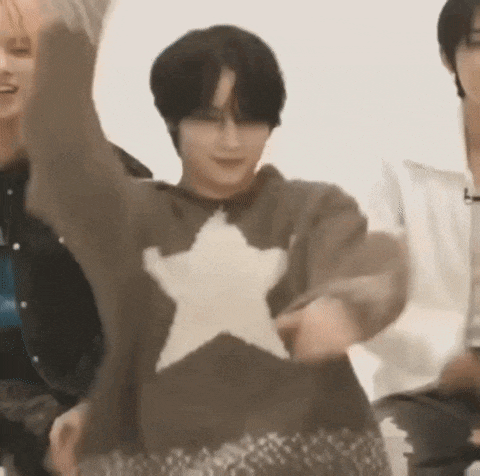a man in a brown sweater with a white star on it is dancing in front of a group of people .