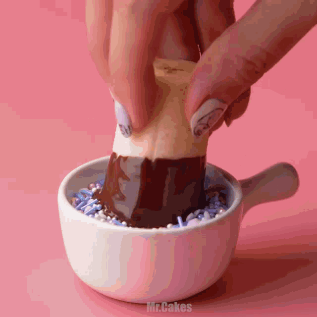 a person dipping an ice cream cone in chocolate and sprinkles in a small white bowl