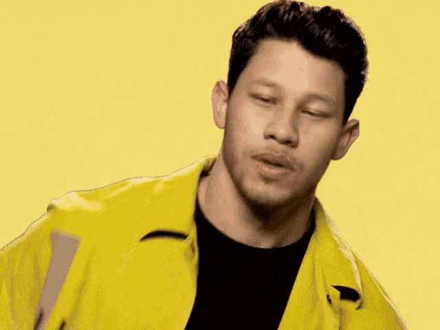 a man in a yellow jacket and black shirt is making a funny face .