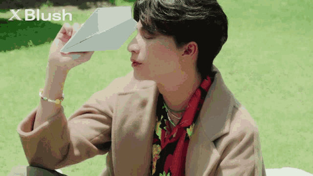 a man is holding a paper airplane in front of his face and the word blush is on the bottom right