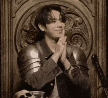 a man in armor sits in a chair with his hands together