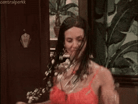 a woman in a red bra is standing in front of a door with her hair covered in feathers .