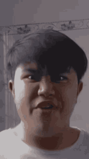 a close up of a young man 's face with a white shirt on