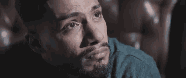 a man with a beard is sitting in a chair with his eyes closed and a sad look on his face .