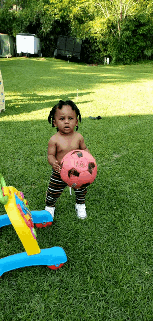 a baby standing in the grass holding a red soccer ball