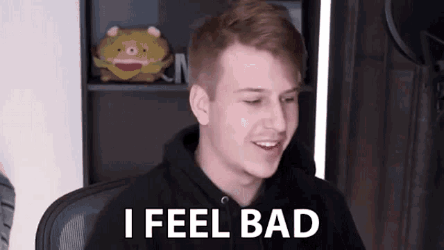 a young man in a black hoodie is sitting in a chair and smiling while saying `` i feel bad '' .