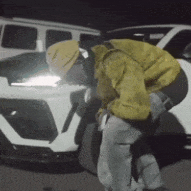 a man in a yellow jacket is kneeling next to a white car