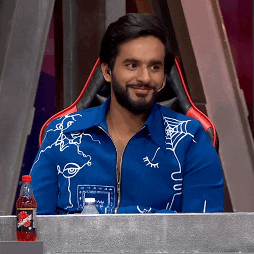 a man in a blue jacket sits at a table with a bottle of dr pepper
