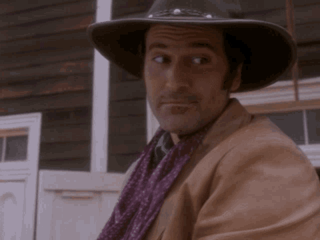 a man wearing a cowboy hat and a purple scarf looks at the camera