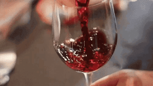 a close up of a person pouring red wine into a glass .