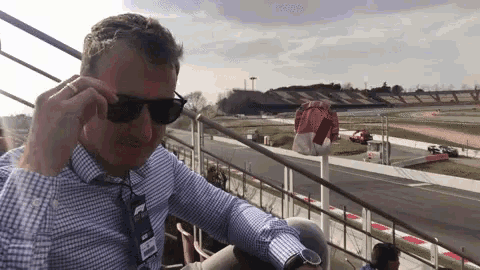 a man wearing sunglasses and a name tag that says ' ferrari ' on it sits in front of a race track