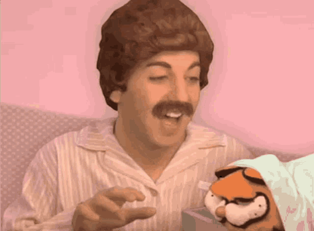 a man with a mustache and a wig is holding a stuffed garfield .