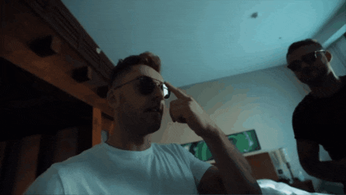 a man adjusts his sunglasses while another man stands behind him