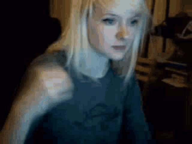 a woman with blonde hair and blue eyes is wearing a black shirt and making a funny face .